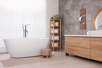 Photo of Stylish bathroom interior with ceramic tub, care products and houseplant