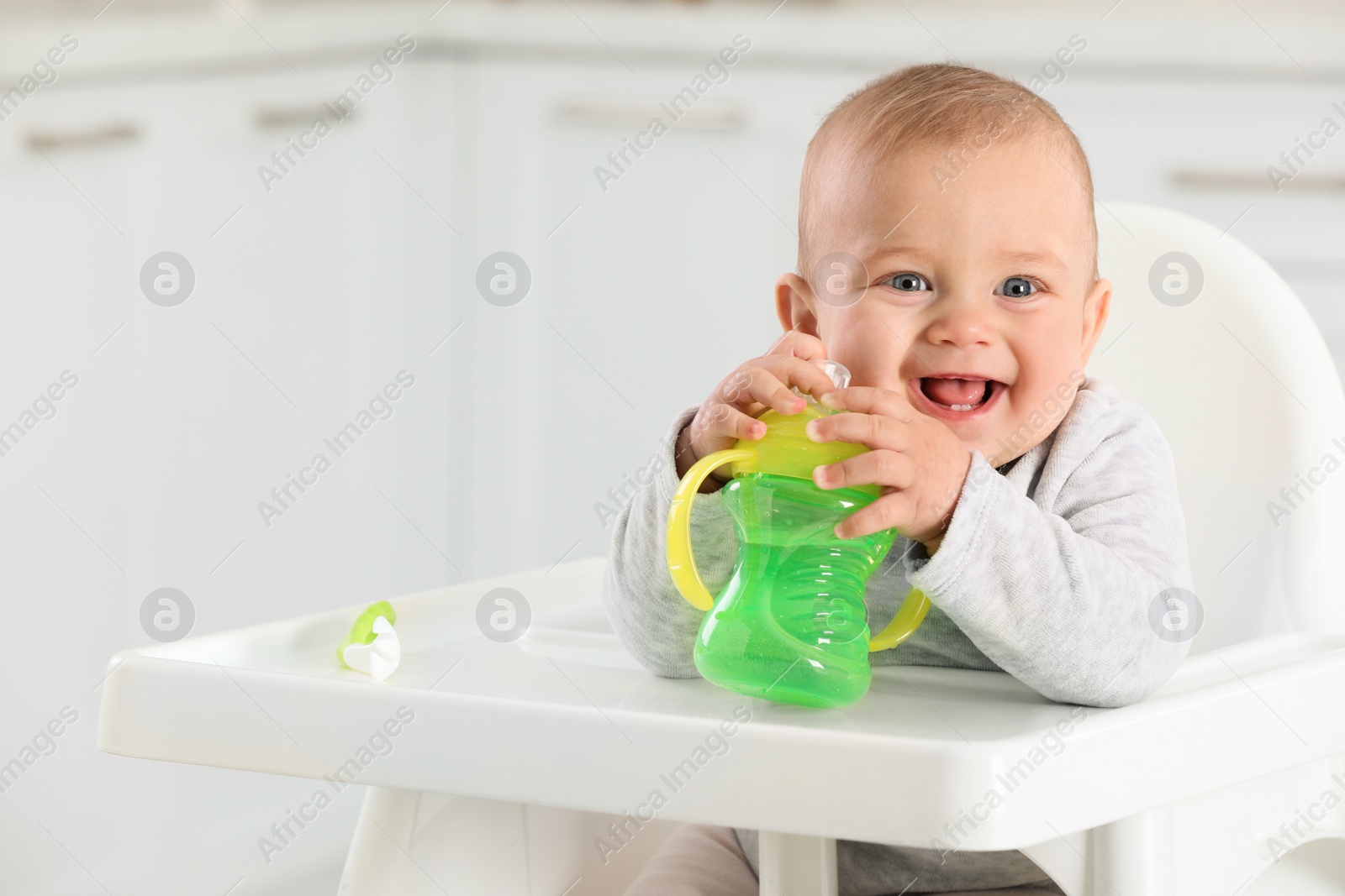 Photo of Cute little baby with sippy cup at home. Space for text