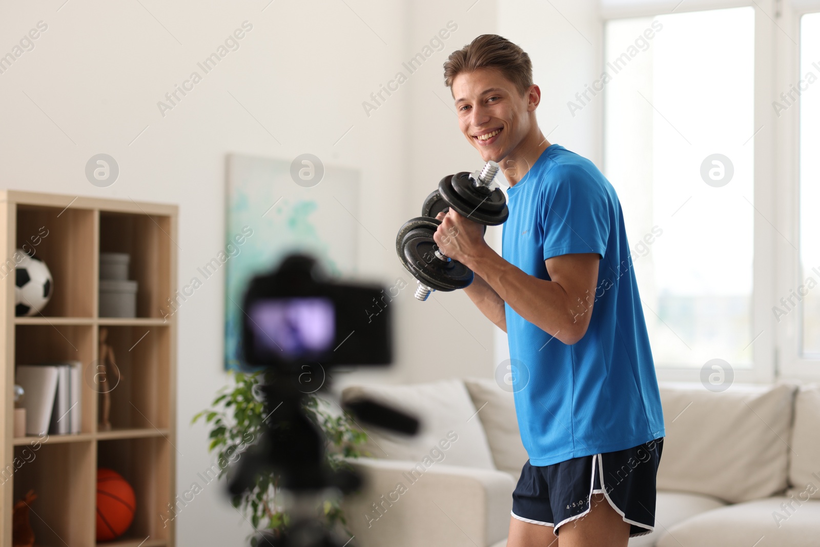 Photo of Smiling sports blogger working out with dumbbells while recording fitness lesson at home