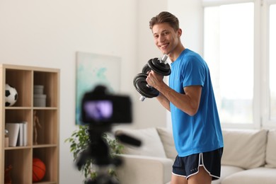 Photo of Smiling sports blogger working out with dumbbells while recording fitness lesson at home