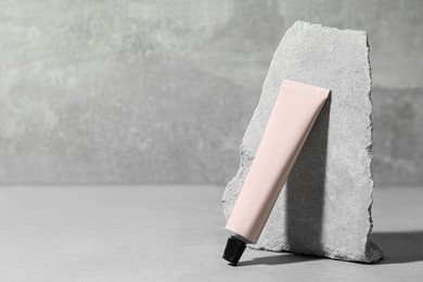 Photo of Tube of hand cream near stone on grey background. Mockup for design