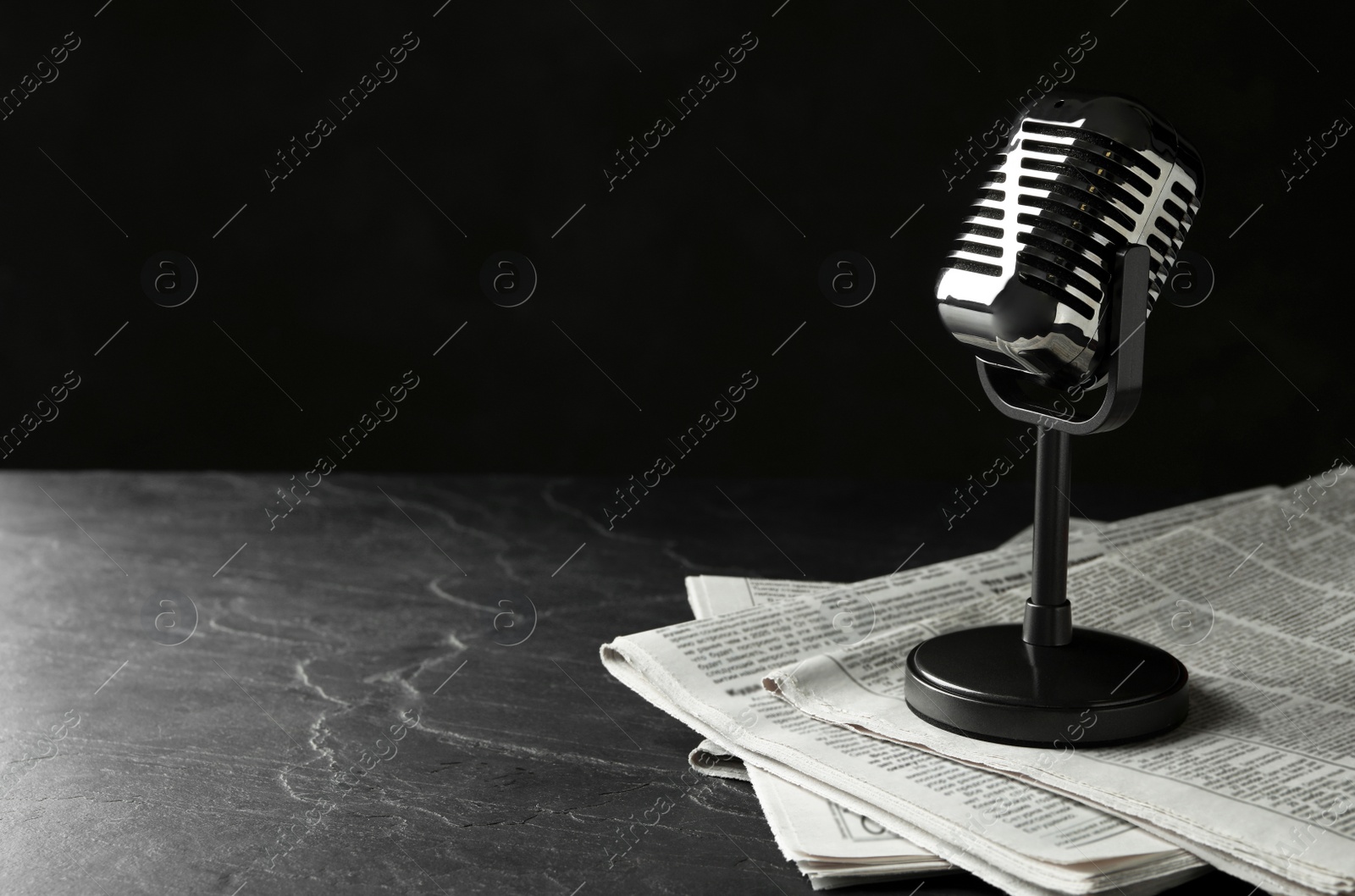 Photo of Newspapers and vintage microphone on dark stone table, space for text. Journalist's work