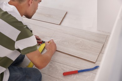 Photo of Professional worker using measuring tape during installationlaminate flooring indoors, closeup