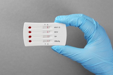 Doctor holding disposable multi-infection express test on light grey background, top view