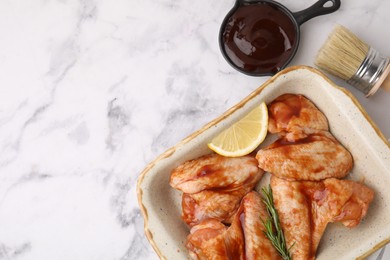 Fresh marinade, basting brush, raw chicken wings, rosemary and lemon on white marble table, flat lay. Space for text