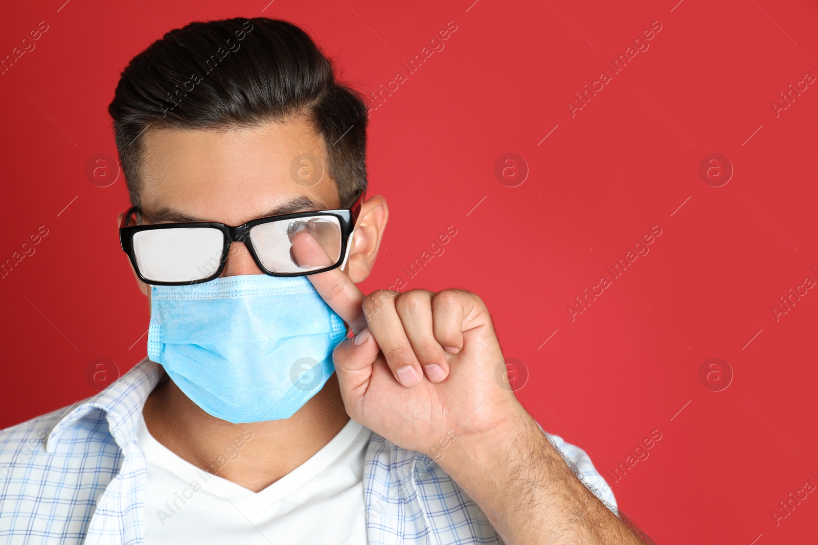 Photo of Man wiping foggy glasses caused by wearing medical mask on red background. Space for text