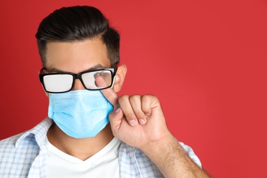 Photo of Man wiping foggy glasses caused by wearing medical mask on red background. Space for text