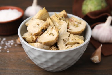 Bowl of pickled artichokes on wooden table, closeup