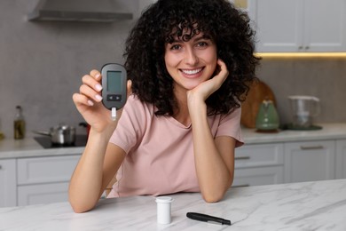 Diabetes. Happy woman holding digital glucometer at white marble table in kitchen