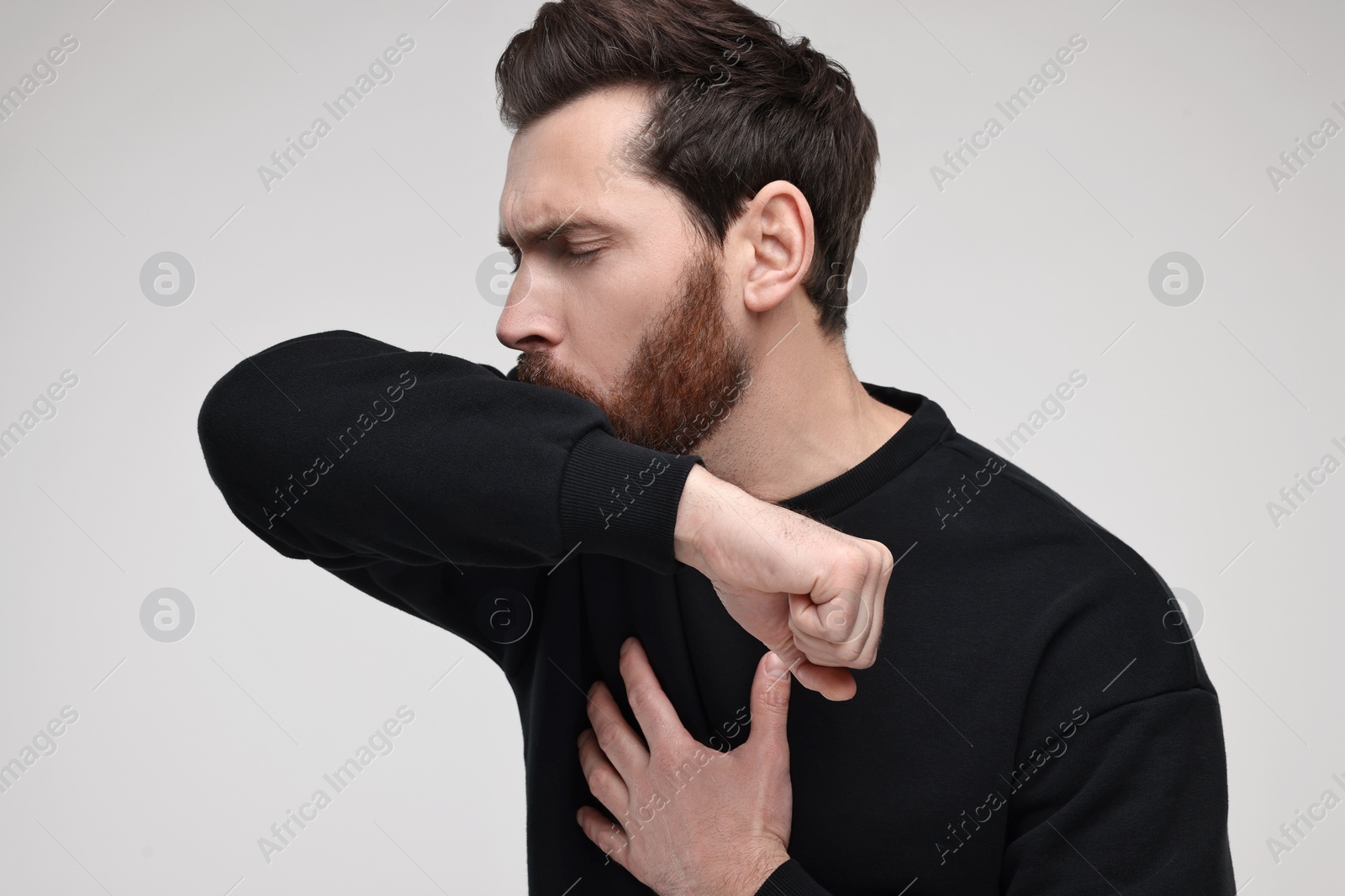 Photo of Sick man coughing into his elbow on light grey background. Cold symptoms