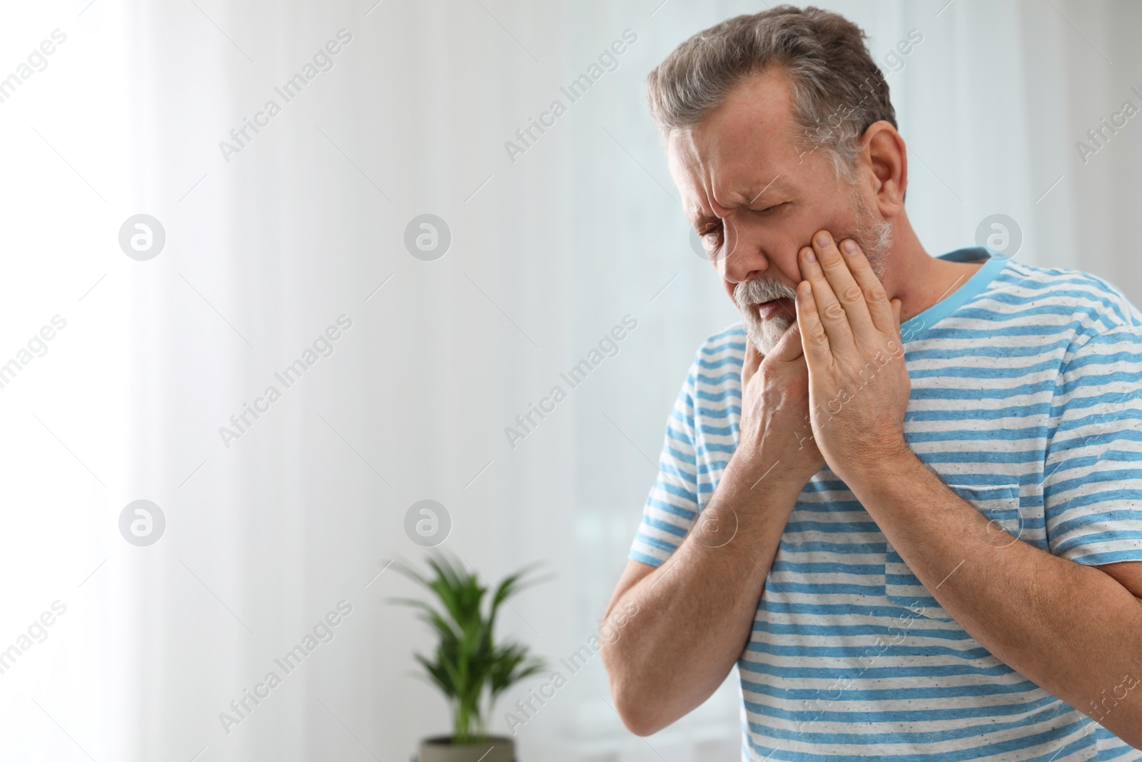 Photo of Mature man suffering from strong tooth pain at home, space for text