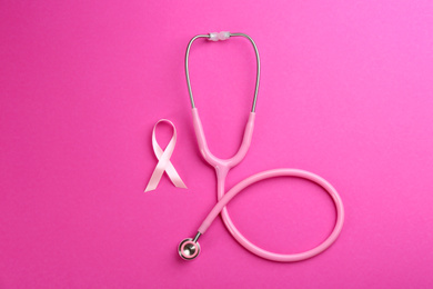 Photo of Pink ribbon as breast cancer awareness symbol and stethoscope on color background, flat lay