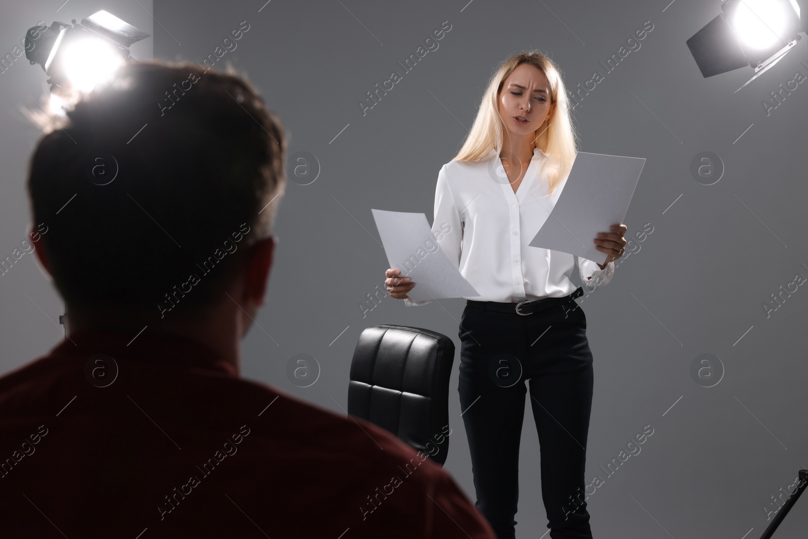 Photo of Emotional woman with script performing in front of casting director against grey background in studio