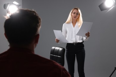 Photo of Emotional woman with script performing in front of casting director against grey background in studio
