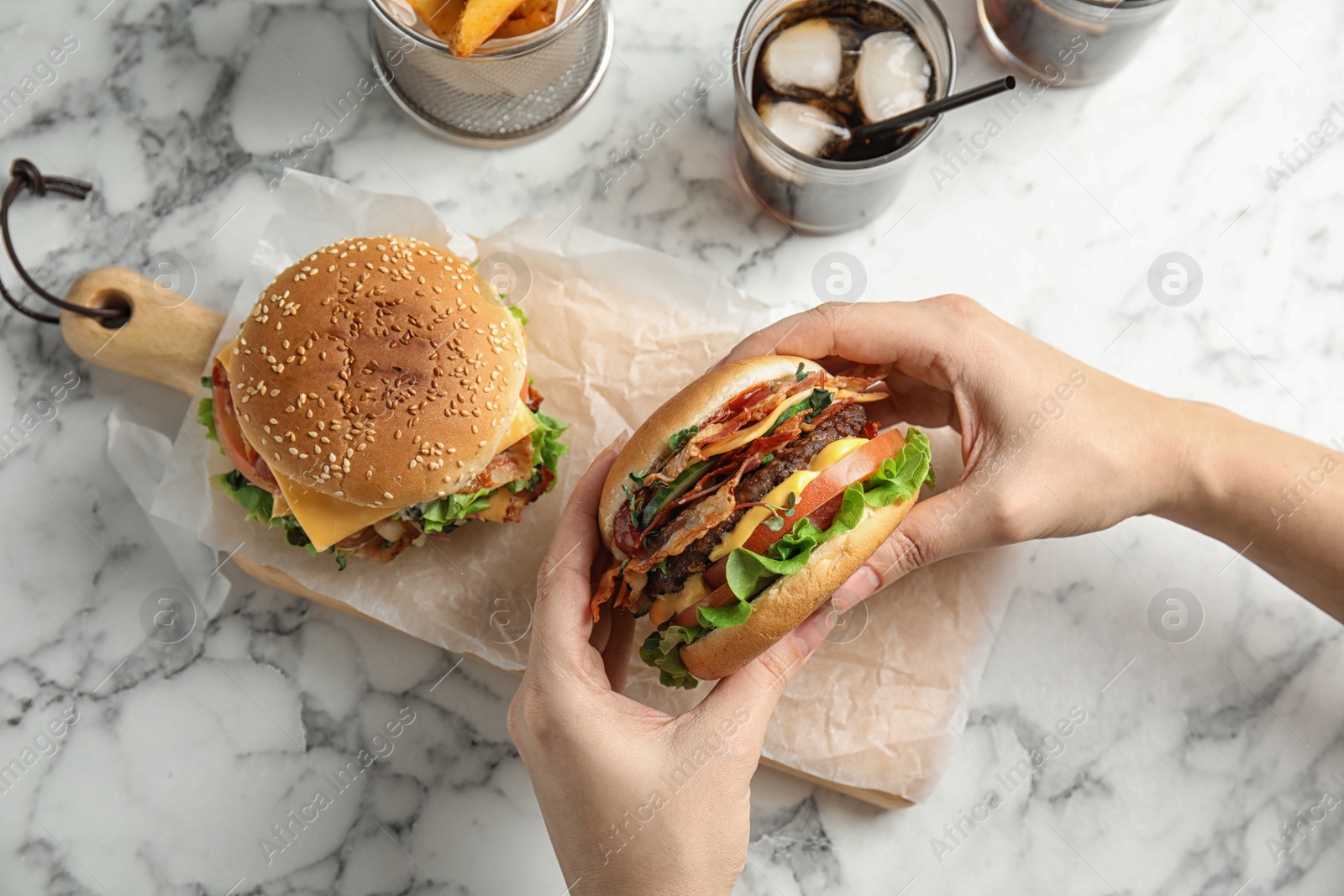 Photo of Woman holding tasty burger with bacon at served table, top view