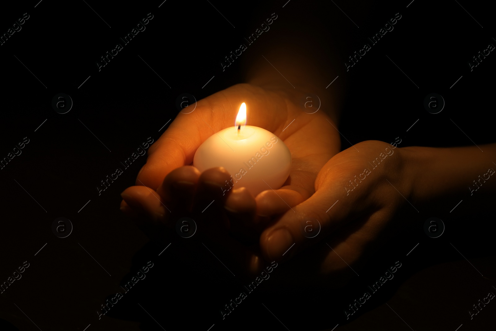 Photo of Woman holding burning candle in hands on black background, closeup