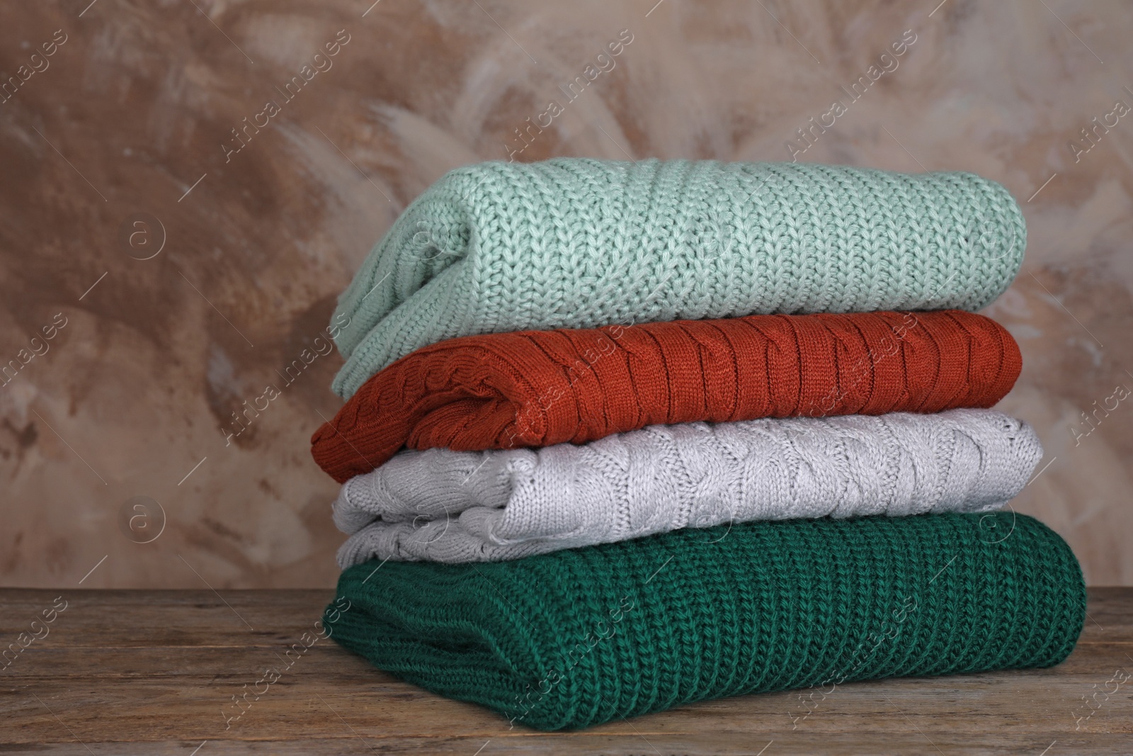 Photo of Stack of folded knitted sweaters on wooden table against brown background