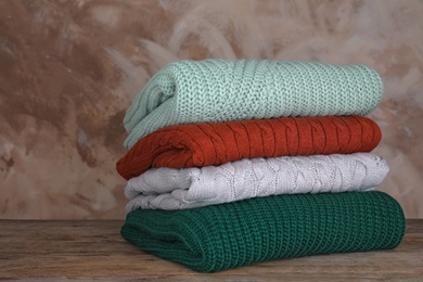 Photo of Stack of folded knitted sweaters on wooden table against brown background