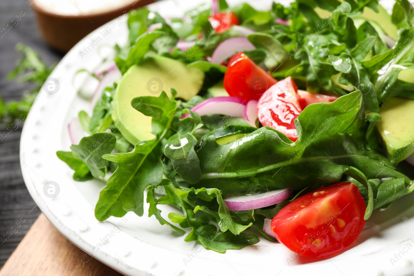 Photo of Delicious salad with avocado, arugula and tomatoes on plate, closeup