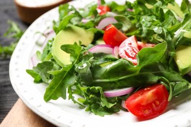 Delicious salad with avocado, arugula and tomatoes on plate, closeup