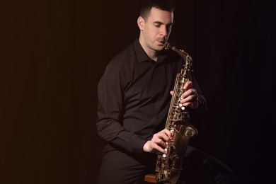 Photo of Young man playing saxophone on dark background. Space for text