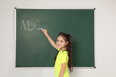 Photo of Little school child writing with chalk on blackboard