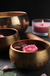 Photo of Tibetan singing bowls with beautiful rose flowers, and burning candle on table, closeup