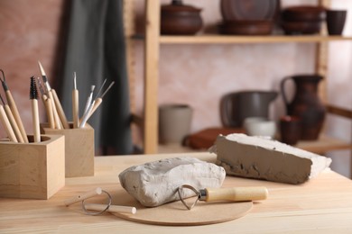 Clay and set of modeling tools on wooden table in workshop