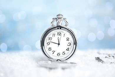 Photo of Pocket watch on snow against blurred lights. New Year countdown