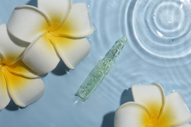 Photo of Skincare ampoule and beautiful plumeria flowers in water on light blue background, flat lay