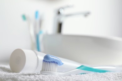 Photo of Plastic toothbrush with paste and tube on white towel in bathroom, closeup. Space for text