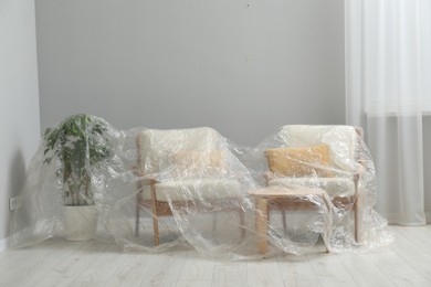 Stylish chairs, table and houseplant covered with plastic film at home
