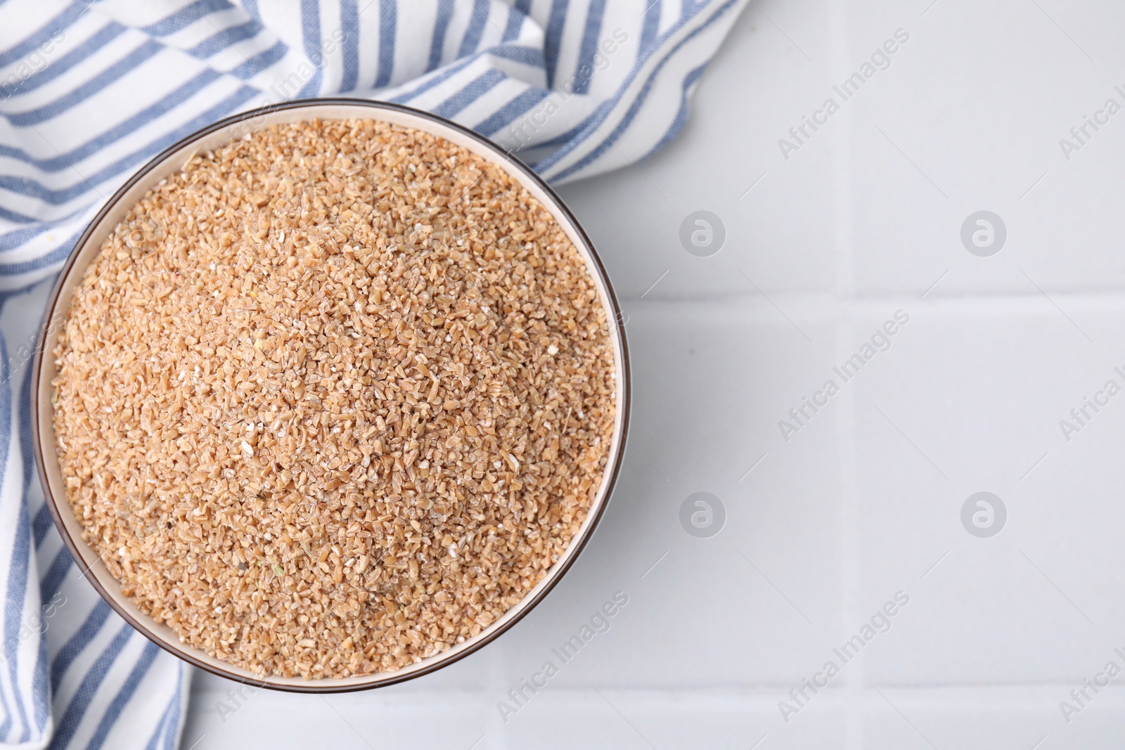 Photo of Dry wheat groats in bowl on white tiled table, top view. Space for text