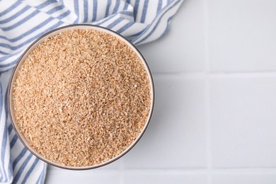 Dry wheat groats in bowl on white tiled table, top view. Space for text