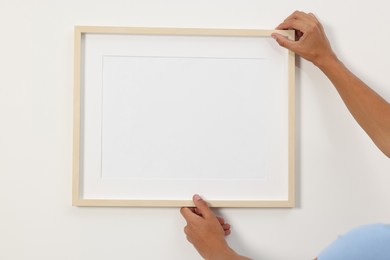 Young man hanging picture frame on white wall indoors, closeup