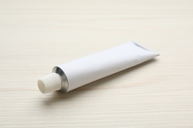 Photo of Blank white tube of ointment on light wooden table. Space for text