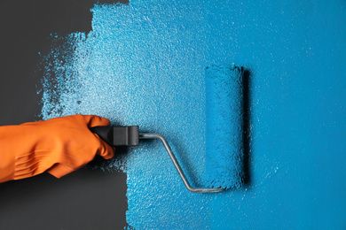 Photo of Woman painting grey wall with blue dye, closeup