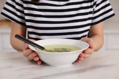 Woman with bowl of tasty soup at white marble table, closeup