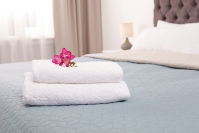 Photo of Stack of fresh towels with flowers on bed in hotel room