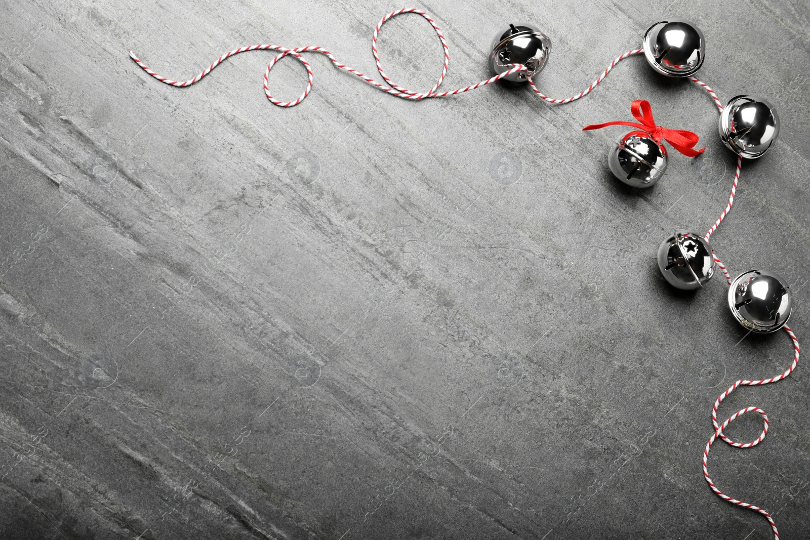 Photo of Shiny silver sleigh bells on grey stone table, flat lay. Space for text