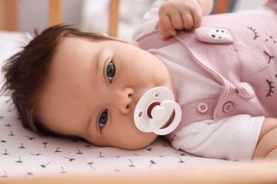 Cute little baby with pacifier lying in comfortable crib at home, closeup. Bedtime