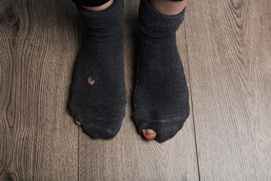 Photo of Poor person in shabby socks on wooden floor, closeup