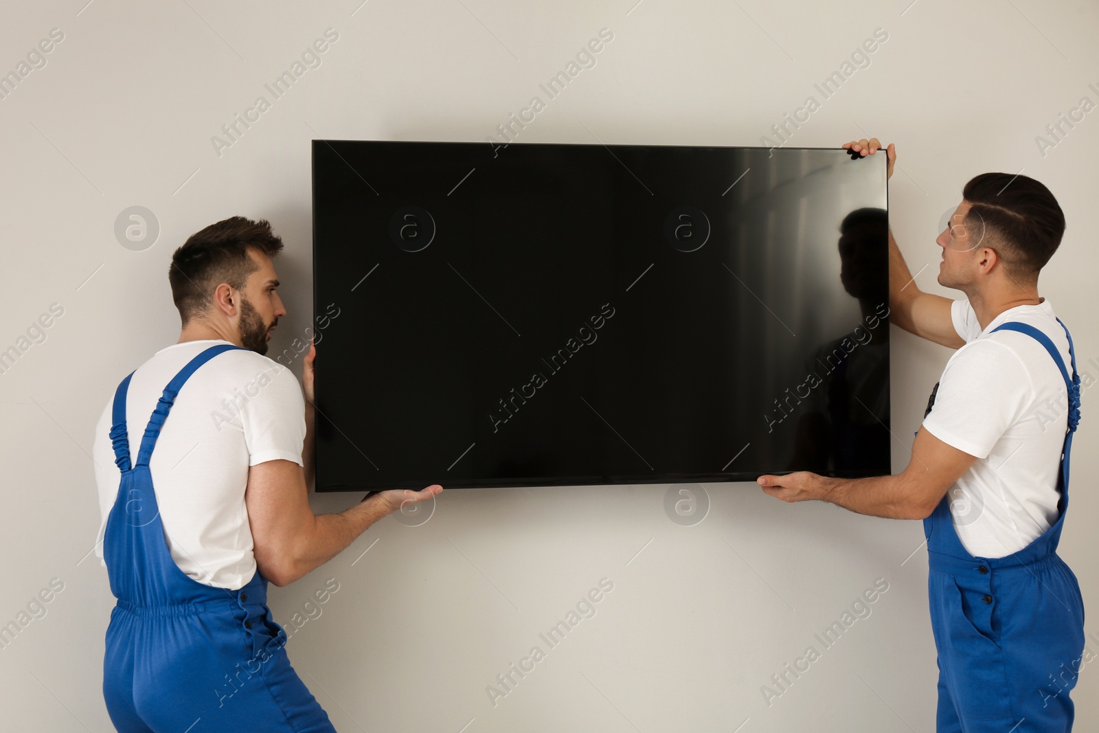 Photo of Professional technicians installing modern flat screen TV on wall indoors