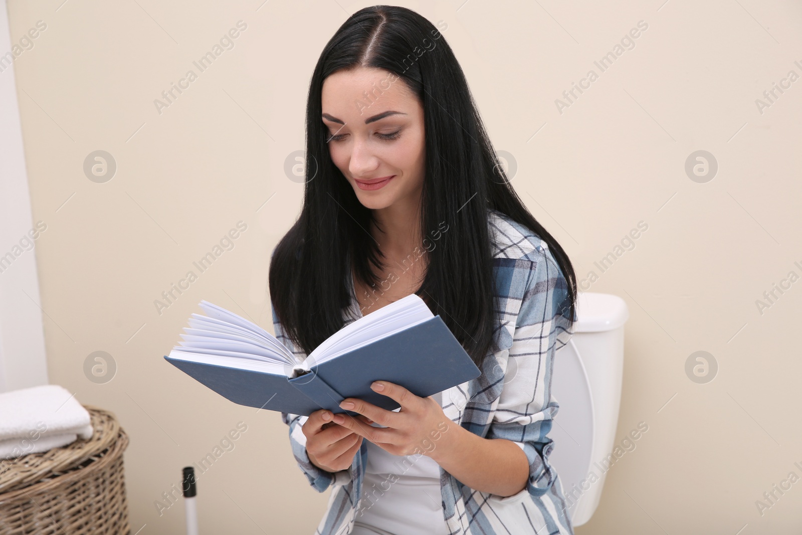 Photo of Woman with book sitting on toilet bowl in bathroom