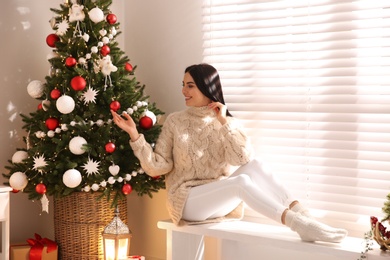 Young woman sitting on bench near Christmas tree at home