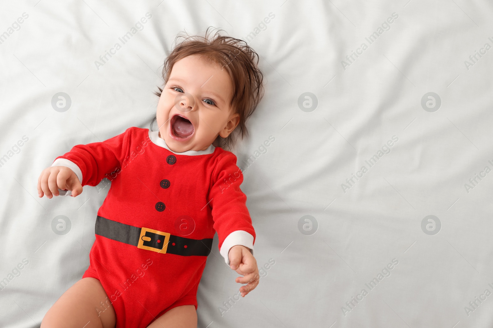 Photo of Cute baby wearing festive Christmas costume on white bedsheet, top view. Space for text