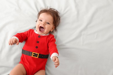 Cute baby wearing festive Christmas costume on white bedsheet, top view. Space for text
