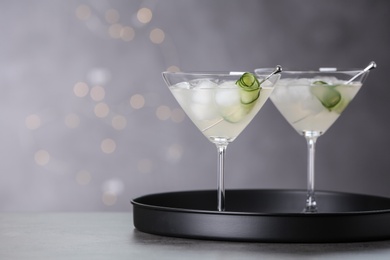 Glasses of martini with cucumber on tray against blurred lights. Space for text