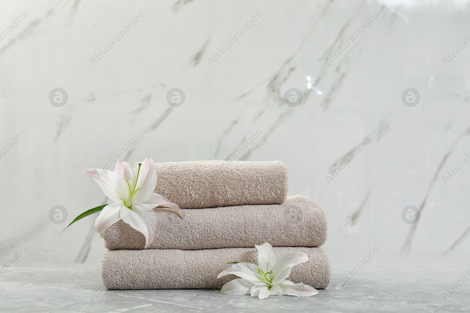 Photo of Stack of fresh towels with flowers on grey table against light background. Space for text