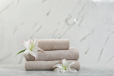 Stack of fresh towels with flowers on grey table against light background. Space for text